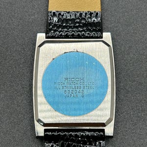 K&ouml;nnte beinhalten: Eine Vintage-Ricoh-Uhr mit einem rechteckigen Edelstahlgeh&auml;use und einem schwarzen Lederarmband. Auf der R&uuml;ckseite der Uhr steht unter anderem "Ricoh Watch Co., Ltd., All Stainless Steel, 632042, Japan Q."