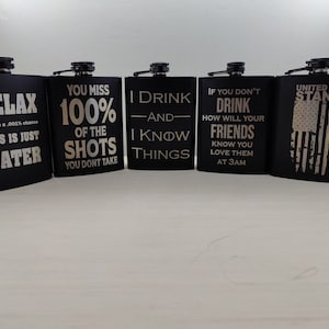 May include: Five black metal hip flasks with various engraved sayings. The sayings include "Relax, This is Just Water", "You Miss 100% of the Shots You Don't Take", "I Drink -And- I Know Things", "If You Don't Drink How Will Your Friends Know You Love Them At 3AM", and "United We Stand".