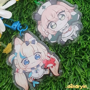 Pode incluir: Dois chaveiros de acrílico estilo anime com personagens de desenhos animados. Um chaveiro retrata um personagem com cabelo rosa e um chapéu de enfermeira. O outro mostra um personagem com cabelo loiro, segurando um caranguejo vermelho. Ambos têm detalhes em azul.