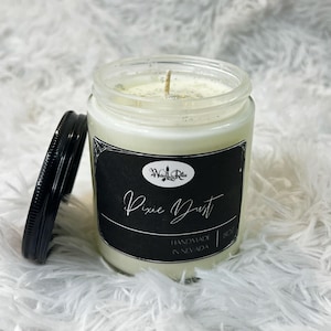 May include: A white candle in a glass jar with a black label that says "Witchy Little Realm" and "Pixie Dust" in cursive. The label also says "Handmade in Nevada" and "8oz".