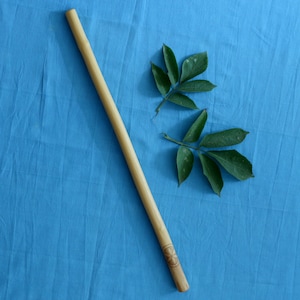 May include: A long, wooden stick with a carved design at the end, lying on a blue fabric surface. Two green leaves are also on the surface.