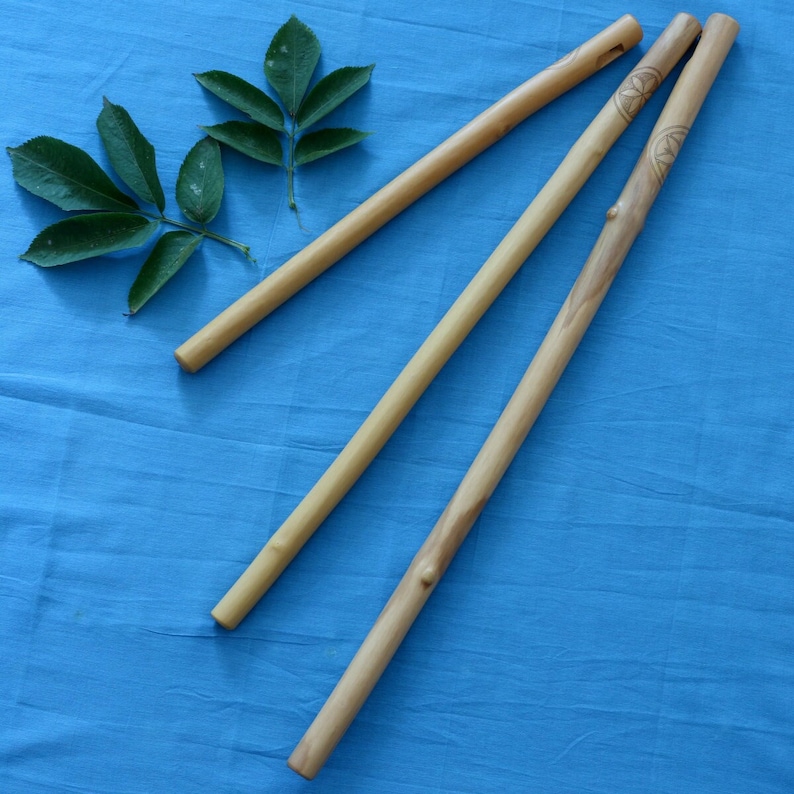 May include: Three wooden staffs with intricate carvings on a blue background. The staffs are made of light brown wood and have a smooth finish.