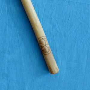 May include: A wooden stick with a geometric design carved into it. The design is a six-pointed star with a circle in the center.