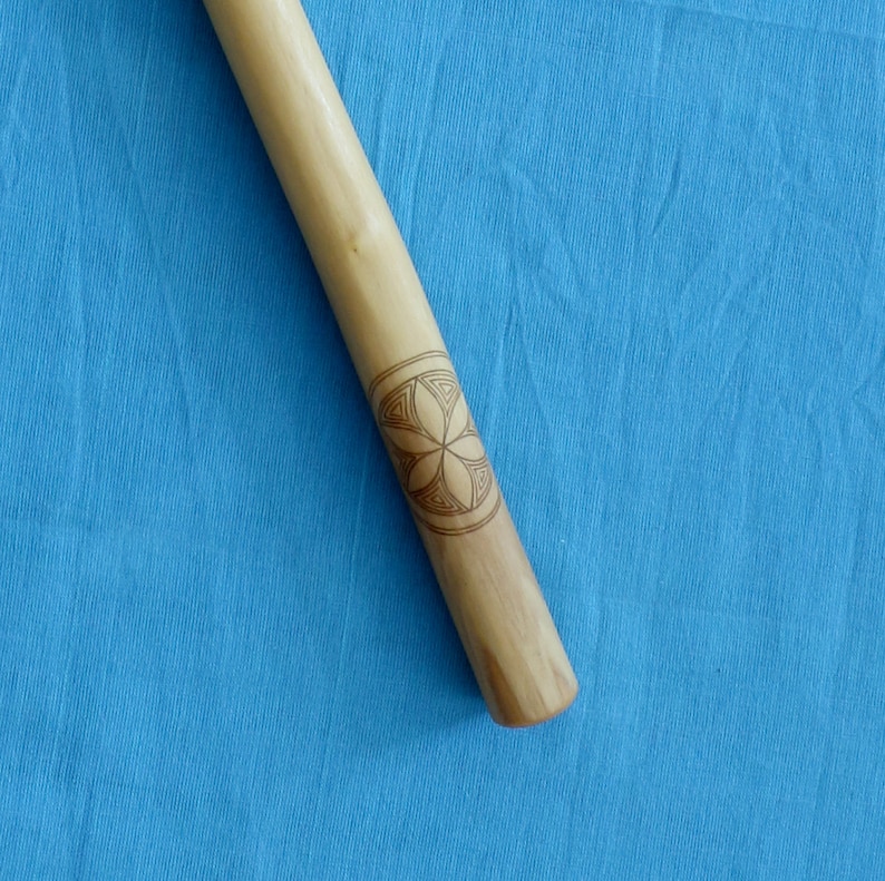 May include: A wooden stick with a geometric design carved into it. The design is a six-pointed star with a circle in the center.