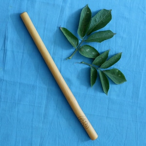 May include: A long, wooden stick with a carved design at one end. The stick is lying on a blue fabric surface. A green leaf is also on the surface.