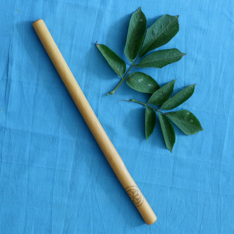 May include: A long, wooden stick with a carved design at one end. The stick is lying on a blue fabric surface. A green leaf is also on the surface.