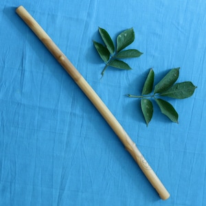 May include: A wooden stick with a carved design on a blue fabric background. Two green leaves are on the fabric.