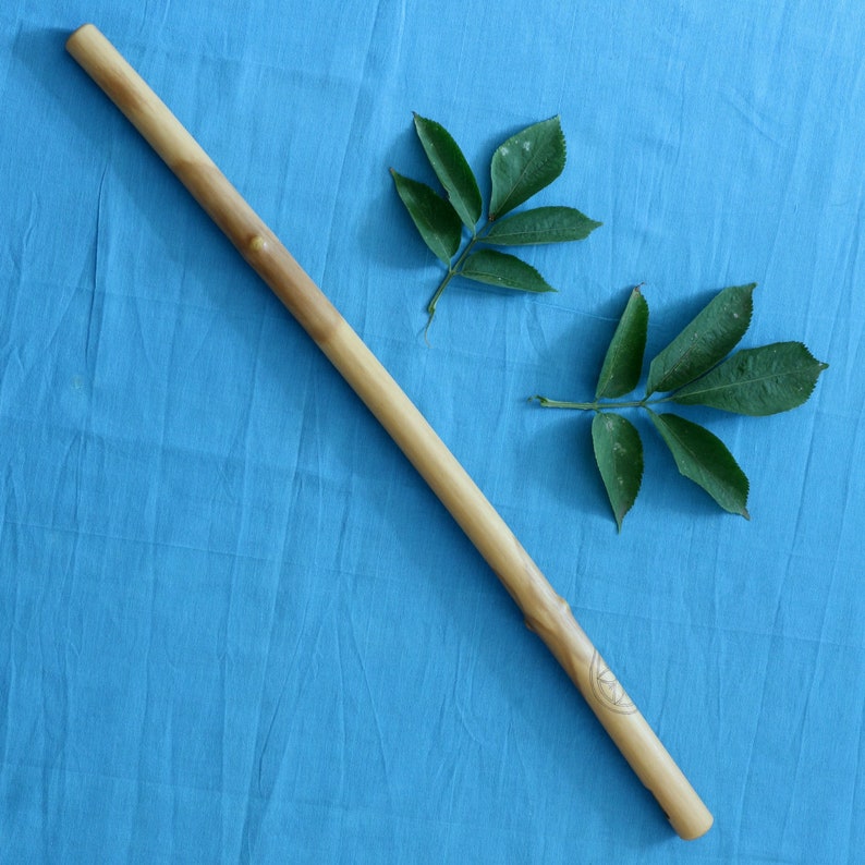 May include: A wooden stick with a carved design on a blue fabric background. Two green leaves are on the fabric.