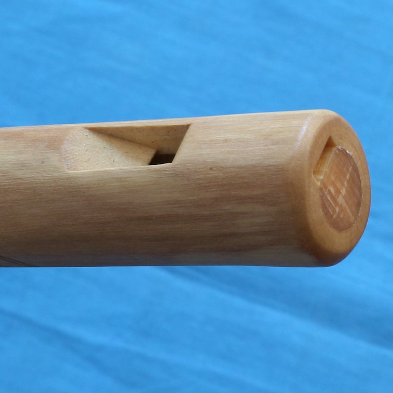 May include: Close-up of the mouthpiece of a wooden flute. The flute is made of light brown wood and has a simple design.