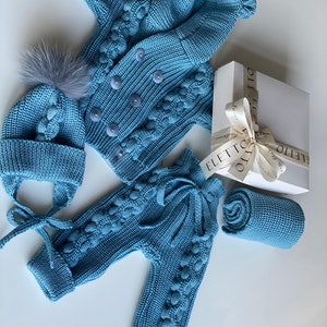 K&ouml;nnte beinhalten: Hellblaues Strick-Outfit-Set f&uuml;r Babys, bestehend aus einer Jacke mit Kn&ouml;pfen, einer Hose mit Bindeb&auml;ndern, einer M&uuml;tze mit Bommel und einer gerollten Decke. Das Set wird mit einer Geschenkbox pr&auml;sentiert.