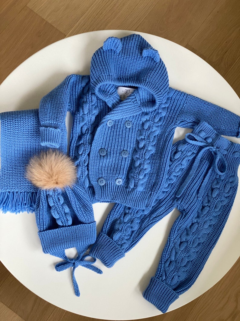 K&ouml;nnte beinhalten: Hellblaues Strick-Outfit-Set f&uuml;r Babys, bestehend aus einer Kapuzenjacke mit B&auml;renohren, einer passenden M&uuml;tze mit Bommel, einem Schal und einer Hose. Das Set hat ein Zopfmuster und Knopfverschl&uuml;sse.
