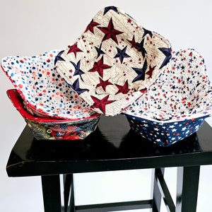 May include: Three fabric bowls with a red, white, and blue star pattern. The bowls are stacked on a black table.