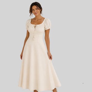 May include: A cream-colored midi dress featuring short puff sleeves, a square neckline with a drawstring tie closure, and a fitted bodice that transitions into a flared, A-line skirt. The garment has a clean, solid-colored fabric construction.