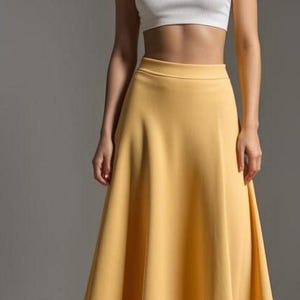 Puede incluir: Una mujer con un top blanco corto y una falda midi amarilla. La falda es de l&iacute;nea A y tiene una cintura alta.