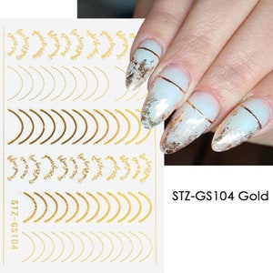 May include: Gold nail art stickers with a variety of designs, including curved lines, small circles, and the words "Live your best life". The sticker sheet is labeled "STZ-GS104 Gold".
