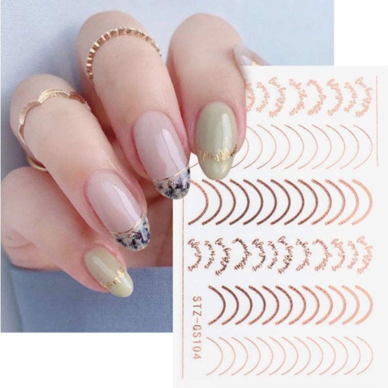 May include: Nail art stickers with a gold and rose gold design. The stickers feature a variety of designs, including a curved line, a floral design, and the words "Believe in Yourself". The stickers are on a white sheet with the text "STZ-GS104".