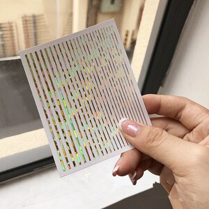 May include: A sheet of iridescent nail art stickers with thin, vertical lines. The lines are a rainbow of colors, including green, yellow, orange, and pink.
