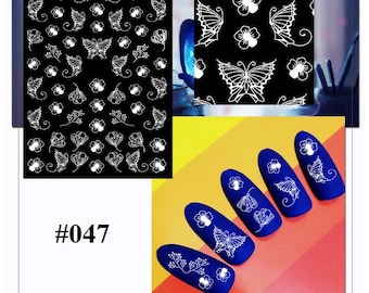 May include: White nail art stickers with a butterfly and flower design on a black background. The stickers are shown on a fingernail. The product number is #047.