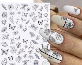 May include: Black and white nail art stickers with butterflies, flowers, and leaves. The stickers are on a white sheet with the number 715 printed at the top.