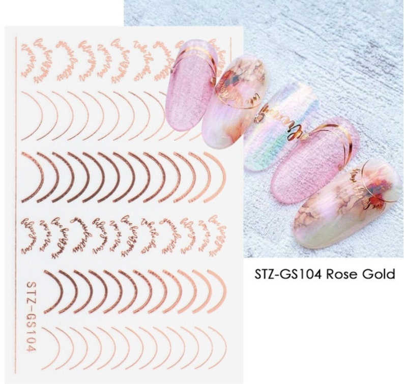 May include: Nail art stickers with rose gold accents. The stickers feature a variety of designs, including curved lines, arches, and the phrase "Love yourself" repeated in a circular pattern. The stickers are labeled "STZ-GS104 Rose Gold".