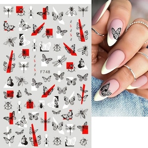 May include: A sheet of nail art stickers with a black and white butterfly design. The stickers are arranged in rows and columns on a gray background. The sheet also includes red accents and the text "F748".