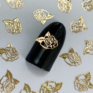 May include: Gold rose nail art decals. The decals are in the shape of roses with leaves. The decals are on a white background.
