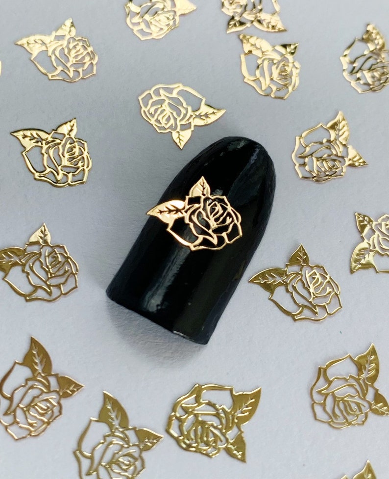 May include: Gold rose nail art decals. The decals are in the shape of roses with leaves. The decals are on a white background.