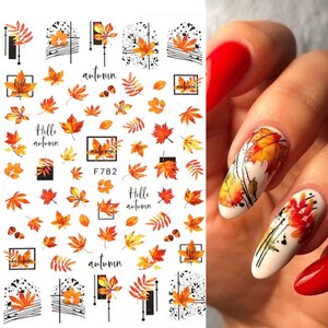 May include: Nail art stickers with a fall theme. The stickers feature orange, yellow, and red leaves, branches, and the words "Hello Autumn".