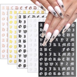 May include: Five sheets of nail stickers with different alphabet letters in gold, black, and white. The letters are in a gothic font style.
