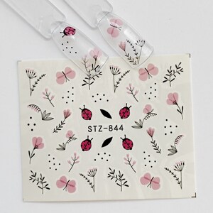 May include: A sheet of nail art stickers with a floral theme. The stickers feature pink flowers, butterflies, ladybugs, and leaves on a white background. The sheet also includes the text "STZ-844".