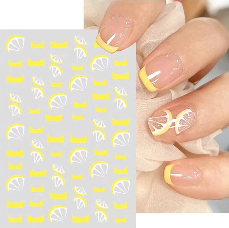 May include: A sheet of nail stickers with a lemon design. The stickers are white and yellow and feature a variety of lemon slices. The sheet is shown next to a hand with nails painted with a yellow and white french manicure.