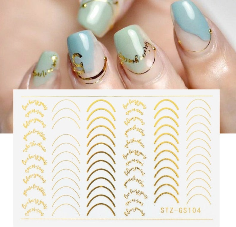 May include: Gold nail stickers with a white background. The stickers feature a variety of designs, including arches, swirls, and the text "Live being you, love is now, believe you can, you're limitless, take the choice". The stickers are labeled "STZ-GS104".