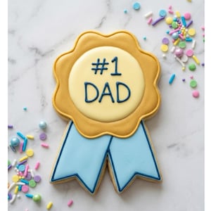 May include: A decorated sugar cookie in the shape of a #1 Dad award. The cookie has a yellow scalloped edge, a light yellow center with the text "#1 DAD" in blue, and light blue ribbons. Colorful sprinkles surround the cookie.