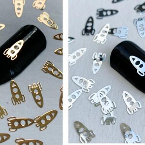 May include: Two black nail polish swatches with silver rocket ship nail art decals. The nail polish swatches are surrounded by silver rocket ship nail art decals.