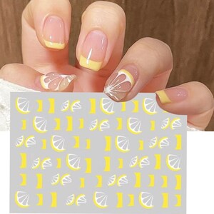 May include: A sheet of nail art stickers with a repeating pattern of white and yellow lemon slices. The stickers are on a gray background.