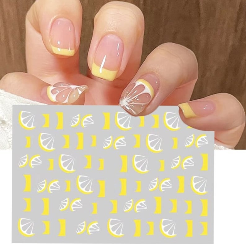 May include: A sheet of nail art stickers with a repeating pattern of white and yellow lemon slices. The stickers are on a gray background.