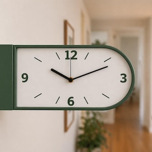 May include: A modern, green and white wall clock with a rectangular base and an oval clock face. The clock features black hands and numerals at the 3, 6, 9, and 12 positions. The clock is mounted on a white wall.