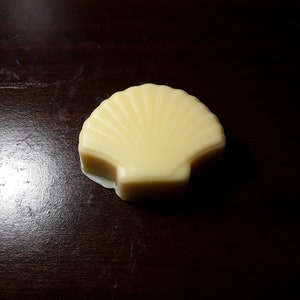 Puede incluir: Una pastilla de jabón blanca con forma de concha sobre una superficie de madera marrón oscura.