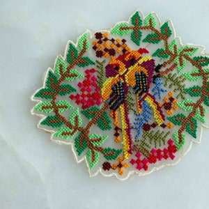 May include: A colorful embroidered patch featuring two birds with green leaves and flowers. The birds are yellow, orange, red, and blue.