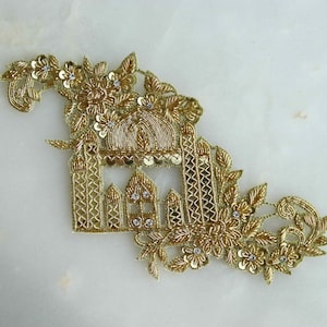 May include: Gold embroidered applique featuring a detailed design of a building with a dome and floral accents.