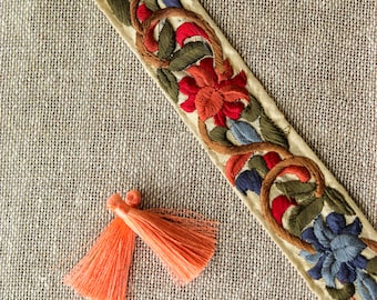 May include: A beige fabric with a floral embroidered trim and two coral tassels.