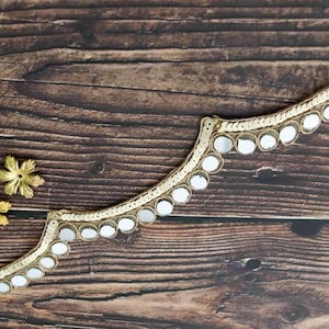 May include: Gold trim with a scalloped edge and round, mirrored accents. The trim is on a brown wooden surface.