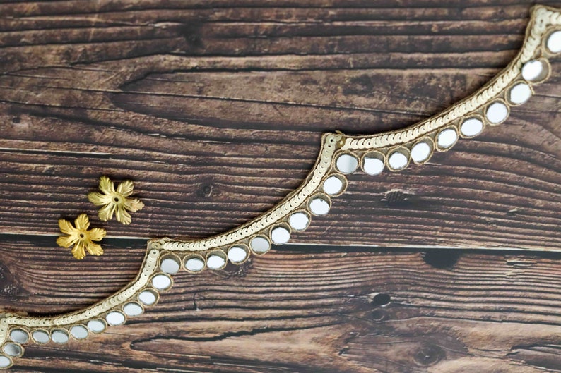 May include: Gold trim with a scalloped edge and round, mirrored accents. The trim is on a brown wooden surface.