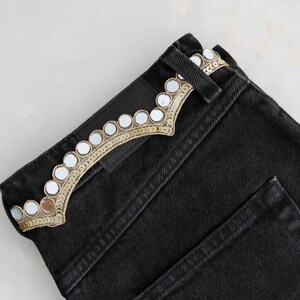 May include: Black denim jeans with a decorative trim of small round mirrors and gold embroidery.