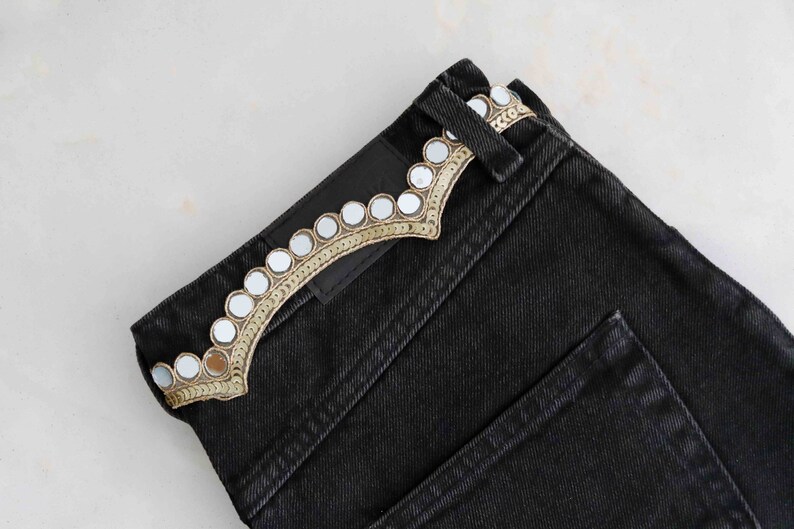 May include: Black denim jeans with a decorative trim of small round mirrors and gold embroidery.