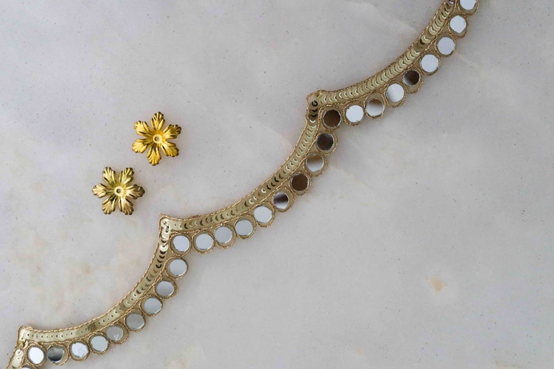 May include: Gold trim with round, mirrored sequins. Two gold flower-shaped embellishments are on the left side of the image.