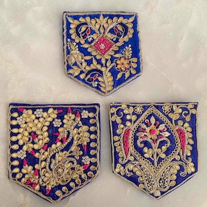 Puede incluir: Tres bolsillos de tela azul con bordados dorados y rosados. Los bolsillos tienen diferentes diseños florales.