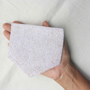 May include: A pentagonal patch featuring a dense, shimmering surface of tiny, light-reflecting silver beads. The patch has a structured, flat shape with clean, stitched edges, creating a textured, metallic appearance that catches the light.