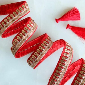 Puede incluir: Borde de terciopelo rojo con lentejuelas doradas y un diseño de hilo dorado. Se incluyen dos borlas rojas.