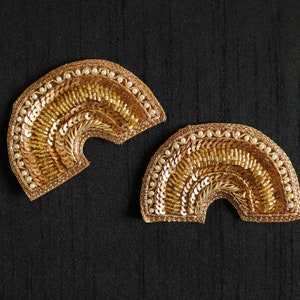 Può includere: Due toppe di tessuto ricamate in oro e bianco a forma di semicircolo. Le toppe sono decorate con paillettes e perline.